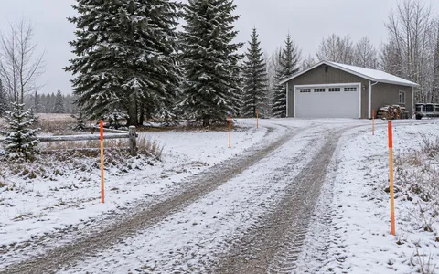 Driveway edge markers beside a rural garage after light snowfall